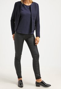 Blazer bleu marine, pantalon en cuir noir ajusté et chaussures noires brillantes. Le blazer présente un design épuré sans fermetures visibles.