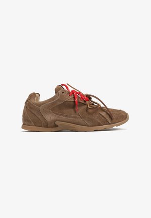 Brązowe zamszowe sneakersy z lekko zakrzywionym designem, czerwonymi sznurowadłami i gumową podeszwą; szczegółowe przeszycia i perforacje po bokach.