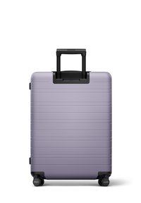 Valise rigide de couleur lavande claire avec des rainures horizontales, poignée rétractable noire et quatre roues pivotantes pour la mobilité.