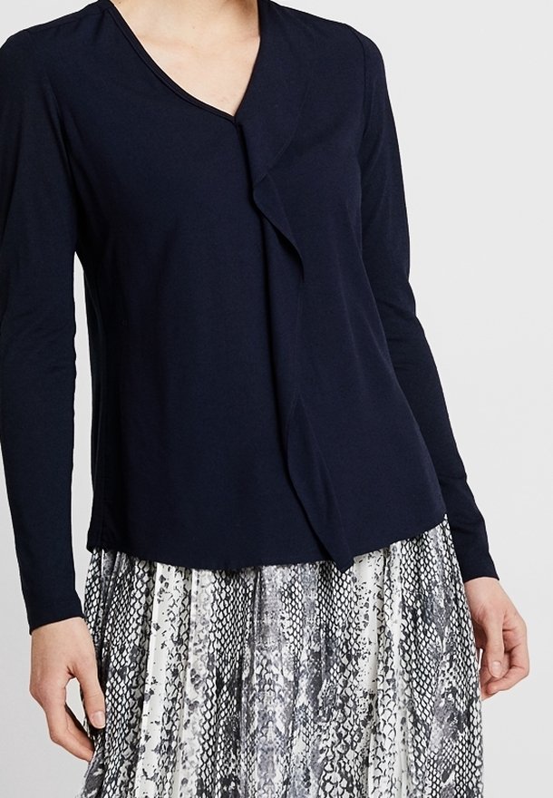 Marinblus med långa ärmar och vikdesign samt v-ringning. Matchad med en silver- och svart mönstrad kjol med orm-mönster, som visar lager av texturer.