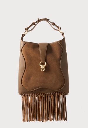 Καφέ δερμάτινη και σουέντ τσάντα με χρυσό κούμπωμα, ρυθμιζόμενο ιμάντα και μακριές φουντίτσες στο κάτω μέρος σε μονόχρωμο φόντο.