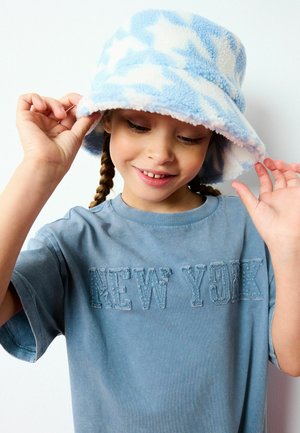 Lichtblauwe bucket hat met een wit sterrenpatroon, gemaakt van zacht fleece materiaal. Blauwe t-shirt met "NEW YORK" geborduurd in donkerblauwe draad.
