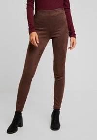 Leggings marron taille haute avec une texture douce ressemblant à du daim. La coupe est près du corps, associée à des bottines à talons noires.