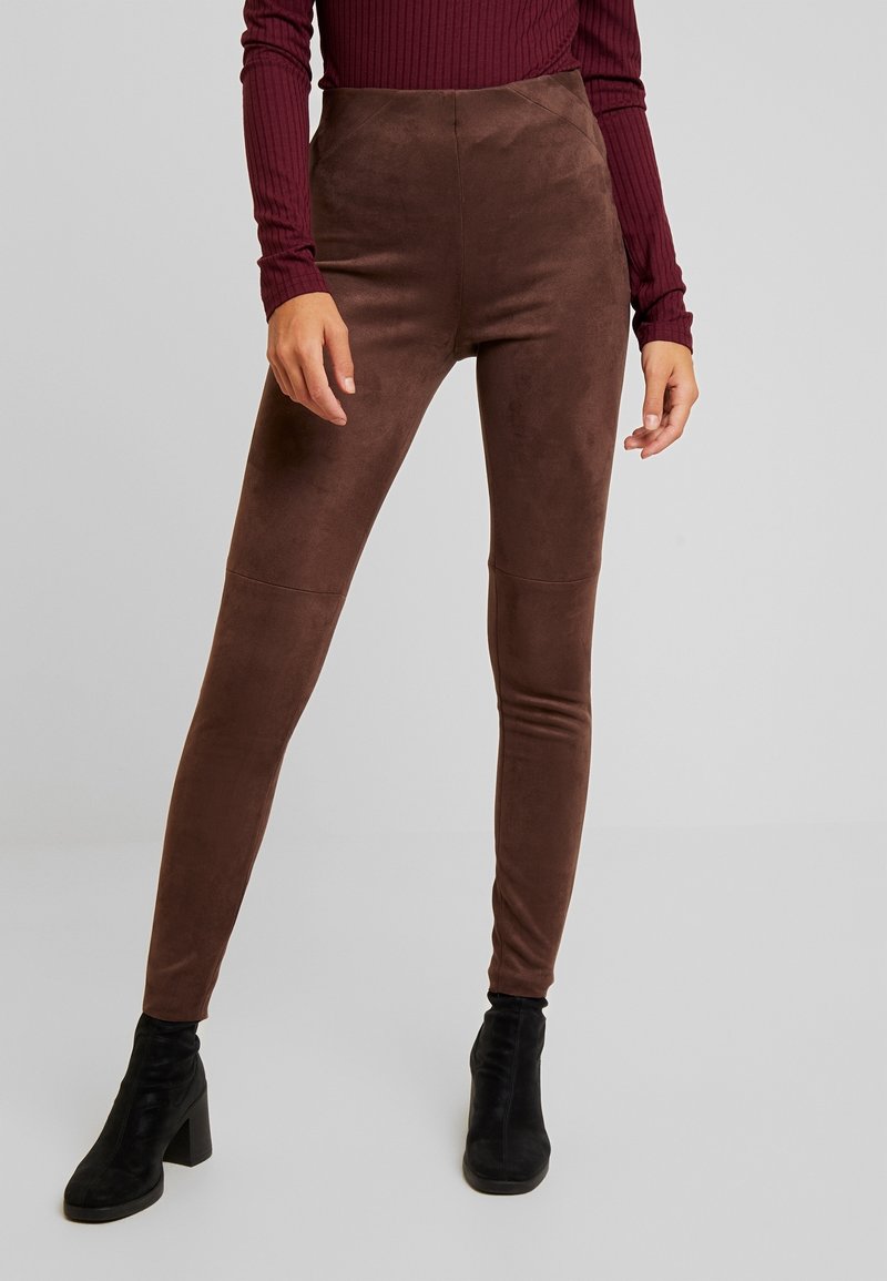 Leggings marron taille haute avec une texture douce ressemblant à du daim. La coupe est près du corps, associée à des bottines à talons noires.