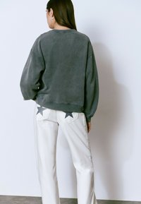 Sudadera gris de corte relajado, combinada con jeans blancos que tienen embellecimientos de estrellas negras en los bolsillos traseros.