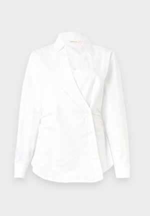 Λευκό γυναικείο πουκάμισο με μακριά μανίκια, front σε στυλ τύλιγμα, κλασικό γιακά και λεπτομέρειες με κουμπιά σε απλό φόντο.