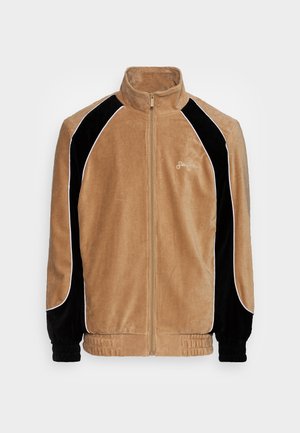 Tan corduroy jacket with black velvet accents, white piping, full zipper, and ribbed cuffs. Features a high collar and loose fit.