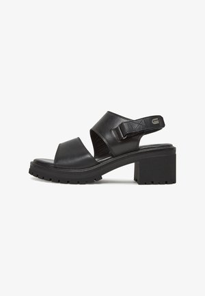 Black block-heeled sandals with a padded ankle strap, open toe, and textured leather upper. Thick, patterned rubber sole for grip.