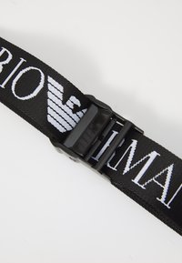Curea împletită neagră cu branding alb, dotată cu o cataramă din plastic negru și o textură netedă; proiectată pentru durabilitate și ajustabilitate.