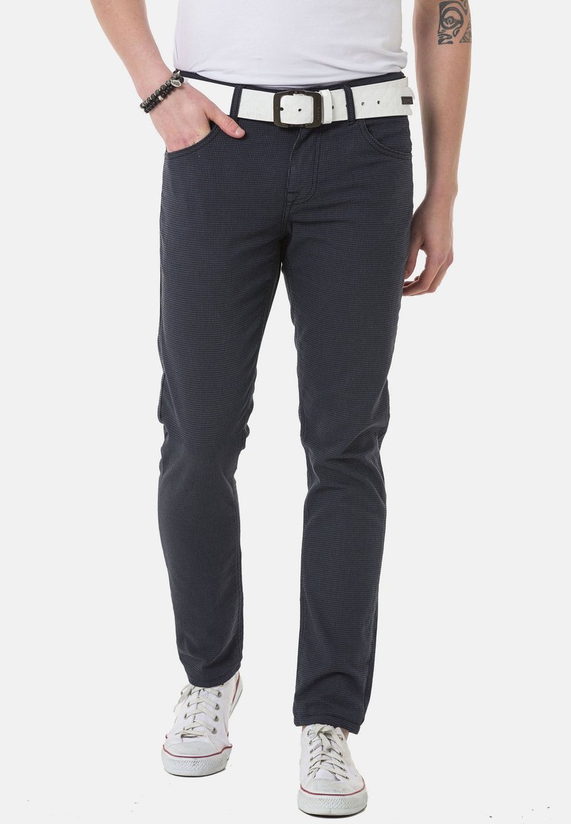 Marineblaue, strukturierte Hose mit schlanker Passform und weißem Gürtel. Verfügt über Taschen vorne und wird mit weißen Sneakers getragen.