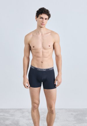 Czarne bokserki Calvin Klein z miękkim pasem w talii, ozdobione białym logo. Materiał jest gładki i dopasowujący się do ciała.