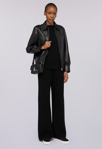 Czarna skórzana kurtka z kołnierzem, połączona z czarnym swetrem i spodniami o szerokich nogawkach. Całość uzupełniają czarne sneakersy z białymi podeszwami.