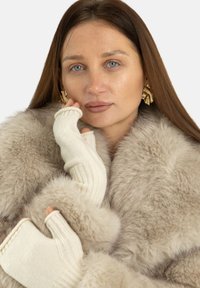 Beżowy płaszcz z futrzanym efektem o puszystej fakturze, zestawiony z kremowymi mitenki bez palców z prążkowanymi detalami. Złote efektowne kolczyki.