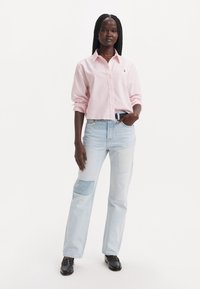 Svetloružová skrátená košeľa na gombíky s dlhými rukávmi, skombinovaná s modrými patchwork džínsami, ktoré majú viaceré textúrované panely a voľný strih.