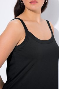 Woman wearing a black sleeveless top with thin straps and silver hoop earrings, shown from shoulders to upper chest against white background.