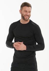Sort langærmet træningsskjorte lavet af glat, strækbart stof. Har en rund halsudskæring og subtil branding på skulderen.