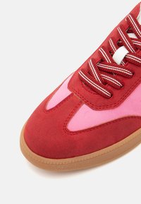 Zapatillas rojas y rosas con materiales de ante y tela, puntera redonda, suela de goma texturizada y cordones a rayas en contraste.