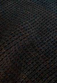 Țesătură texturată de culoare închisă, cu un model țesut în nuanțe de negru și maro, având o suprafață moale și pufoasă.
