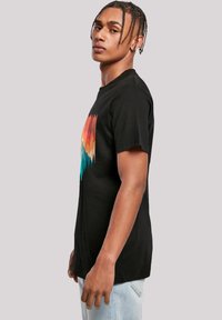Black cotton t-shirt featuring a colorful graphic of orange, red, and teal mountains with black tree silhouettes. Standard crew neck design.