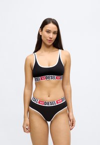 Bralette de algodão preto e cueca de biquíni combinando com detalhes brancos. Apresenta uma faixa elástica larga com a marca "DIESEL" em vermelho e preto.