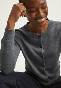 Cardigan grigio lavorato a maglia con colletto tondo, polsini a costine e chiusura con bottoni. Tessuto morbido, design aderente e leggero lucido.