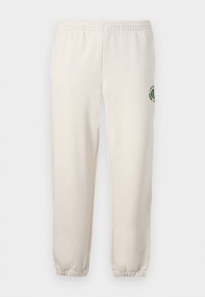 Sweatpants beige claros feitos de algodão, com um cós elástico, punhos canelados e um logótipo verde com desenho de folha na perna esquerda.
