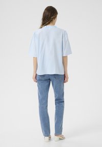 Blouse en coton bleu clair avec des manches bouffantes courtes et un col volanté, associée à un jean droit bleu clair. Texture lisse, coupe décontractée.