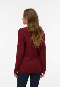 Bordowy sweter z dzianiny z długimi rękawami, o prążkowanej strukturze i luźnym kroju. Tył ma zaokrąglony dół i subtelne detale przeszyć.