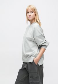 Ανοιχτό γκρι φούτερ με λαιμόκοψη crew, χαμηλωμένους ώμους και ριμπ μανσέτες. Συνδυασμένο με σκούρο γκρι cargo παντελόνι με πολλαπλές τσέπες.