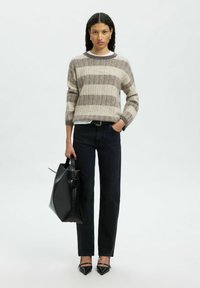 Femme portant un pull rayé beige et gris, un jean noir, des escarpins noirs à bout pointu, tenant un sac à main en cuir noir avec un détail en rose.
