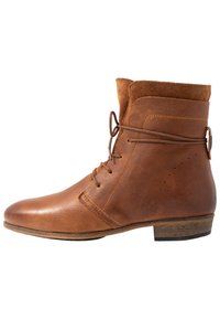 Bottine en cuir brun avec des accents en daim, à bout rond, à lacets et à talon en bois bas. Présente des perforations décoratives sur le côté.