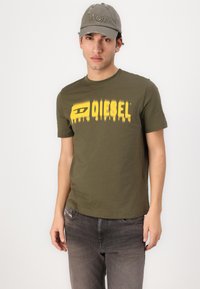 Olive green cotton t-shirt featuring a yellow "DIESEL" logo with a gradient effect. Gray cap with "Won" embroidery. Slim-fit jeans.