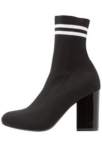 Bottine de style chaussette noire avec texture côtelée, accents de rayures blanches en haut et un talon bloc brillant.