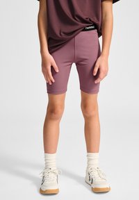Korte sportieve shorts in mauve met een zwart elastische tailleband waarop de merknaam staat. Draag ze met witte sneakers en romige sokken.