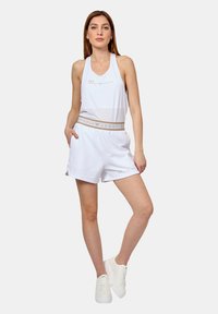 Vit ärmlös tanktopp med "EA7 EMPORIO ARMANI"-logga, tillsammans med matchande vita shorts med elastisk midja. Vita sneakers.