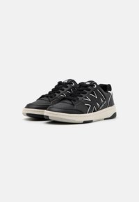 Sorte sneakers laget av lær med kontrasterende hvite detaljer. Rund tå, polstret krage, svarte snørebånd og en teksturert gummisåle.