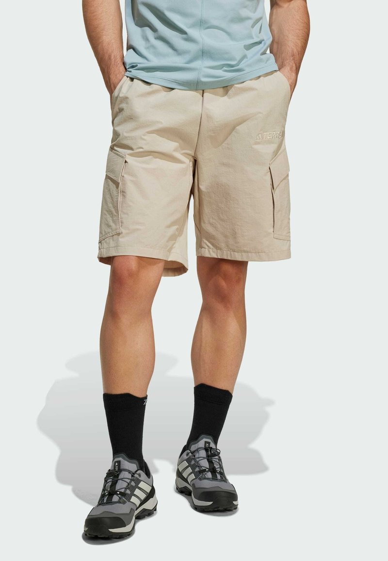 Beige cargo shorts made of lightweight fabric with two side pockets, worn with gray athletic shoes and black crew socks.