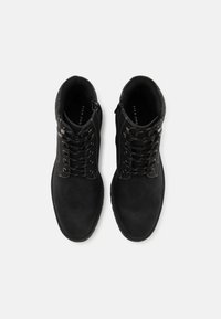 Botas de ante negras con cuello acolchado, ojales de metal, cordones redondos y cremallera lateral. Suela de goma plana con agarre texturizado.