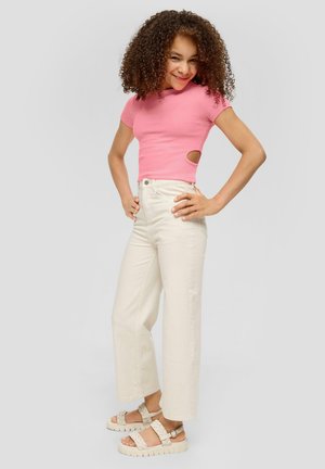 Rosa Kurzarmoberteil mit Cut-Out-Details, kombiniert mit cremefarbenen, hochgeschnittenen, weiten Jeans und beigen Sandalen mit geflochtenem Riemen und dicker Sohle.