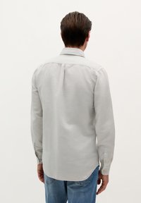 Lys grå langærmet skjorte med skjortekrave, rund kant og gule knapper, parret med blå denim jeans.