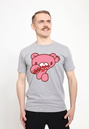 Mand med overskæg iført grå t-shirt med grafik af en lyserød bjørn, der holder en bidt donut med rød fyldning tæt ved munden.