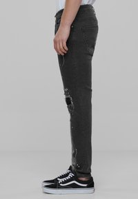 Sorte denimjeans med slim fit, med slitte knedetaljer og hvite malingssprut. Kombinert med svarte lerrets sneakers.
