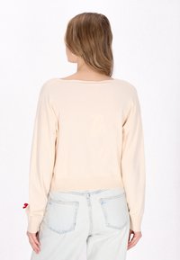 Maglione beige chiaro con una vestibilità morbida, orlo a costine e maniche lunghe. Presenta una scollatura a barco e una texture sottile. Abbinato a jeans chiari.
