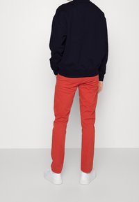 Sudadera azul marino oscura, chinos rojos ajustados y zapatillas blancas, vistos desde atrás. Tejido suave, colores sólidos y diseño minimalista.