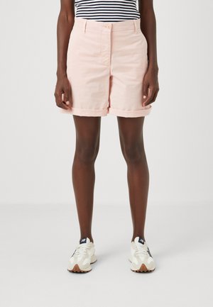 Hellrosa Baumwollshorts mit umgeschlagenen Säumen, ausgestattet mit einem Knopfverschluss und Taschen, kombiniert mit weißen und beigen Sportschuhen.