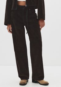 Ruske korduroy-housut, joissa on löysä istuvuus, kiristettävät vyötärönauhat ja sivutaskut. Tekstuuri on pehmeä ja värit ovat hillittyjä.