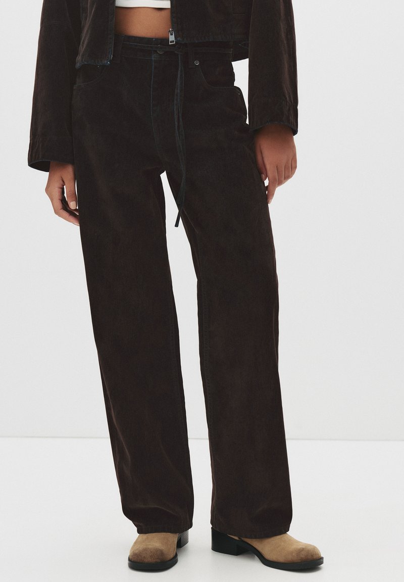 Ruske korduroy-housut, joissa on löysä istuvuus, kiristettävät vyötärönauhat ja sivutaskut. Tekstuuri on pehmeä ja värit ovat hillittyjä.