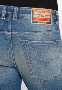 Jeans de denim azul desgastado con una cintura de media altura, costuras visibles y una etiqueta rectangular en la parte posterior, que muestra información de la marca.