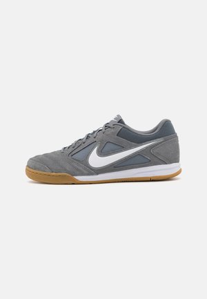 Szary i niebieski but sportowy Nike z białym logo Swoosh, gumową podeszwą i sznurowadłami, pokazany z boku na białym tle.