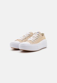 Beige canvas sneakers med vita gummisulor, rund tå och snörning med öglor. Har en upphöjd sula och enkel varumärkeslogotyp på tungan.